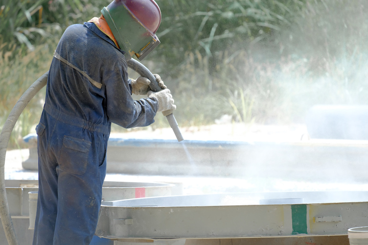 Pracownik usuwa farbę za pomocą piaskowania pod ciśnieniem powietrza